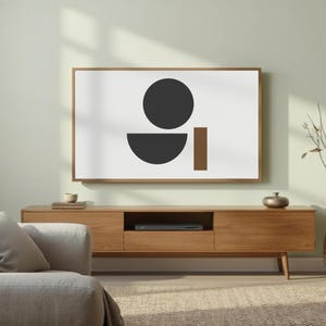 May include: A modern living room featuring a wooden media console with a framed abstract art piece. The artwork displays a black circle, a semi-circle, and a brown rectangle on a white background. A gray sofa and decorative vase complete the scene.