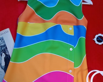 May include: A sleeveless shift dress featuring a vibrant, multi-colored wavy pattern in blue, green, orange, yellow, and pink. The dress has a vertical side panel accented with four small, white, flower-shaped buttons along the front right side.