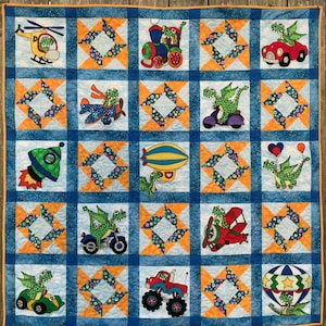 Op de afbeelding: Een blauwe en oranje patchworkdeken met verschillende cartoon-draken in verschillende voertuigen en omgevingen. De deken bestaat uit 16 vierkanten, elk met een ander ontwerp. De ontwerpen omvatten een draak in een luchtballon, een draak in een raket, een draak in een trein, een draak in een auto, een draak in een motorfiets, een draak in een vliegtuig, een draak in een helikopter en een draak in een scooter.