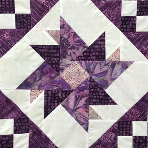 May include: Purple and white quilt block with a geometric pattern. The block is made up of squares and triangles, and the fabric has a floral print.