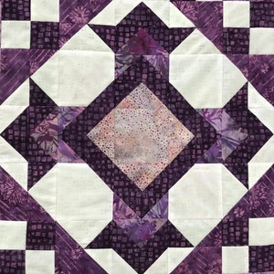 May include: Close-up of a quilt with a geometric pattern. The design features white, purple, and dark purple squares and diamonds. The quilt has a patchwork design with a central diamond shape.