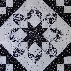 May include: Black and white quilt block with a star design in the center. The star is surrounded by smaller squares with different patterns, including musical notes, swirls, and polka dots.