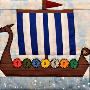 May include: A brown and blue quilted fabric Viking ship with a red sail and a row of round, colourful, embroidered runes along the bottom.