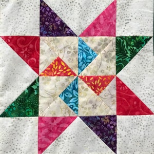 May include: A patchwork quilt block with a star design. The star is made of eight triangles in various colors, including red, pink, purple, green, blue, and orange. The background is white with a subtle speckled pattern.