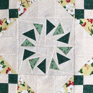 以下が含まれることがあります： 緑と白の花柄のキルトブロック。ブロックは小さな正方形と三角形で構成されており、ブロックの中央には星形のデザインが施されています。