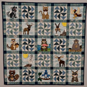 Peut inclure: Une courtepointe bleue et blanche avec une variété d'applications d'animaux, notamment un loup, un chat, un oiseau, un cerf, un écureuil, un ours, un élan, un castor, un lynx et un oiseau. La courtepointe est composée de carrés avec un motif de moulin à vent dans chaque carré.