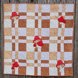 May include: A beige and brown patchwork quilt with a checkered pattern. The quilt is decorated with red and white mushroom appliques.