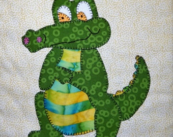 May include: A green and yellow appliquéd alligator with a striped belly and a pink flower on its snout.