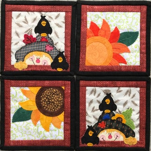 Pode incluir: Quatro  tapetes quadrados de tecido com tema de outono. Cada tapete apresenta um design diferente: um espantalho com um pássaro preto, um girassol, um espantalho com um pássaro preto e um girassol. Os tapetes são emoldurados com uma borda preta e uma borda vermelha.