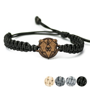 Puede incluir: Pulsera trenzada negra con un dije de madera en forma de oso. El dije es un diseño geométrico de la cara de un oso. La pulsera está disponible en negro, gris y beige.