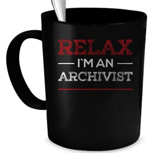 May include: Black coffee mug with white text that reads "Relax I'm an Archivist" in a distressed font. The text is in red and white.