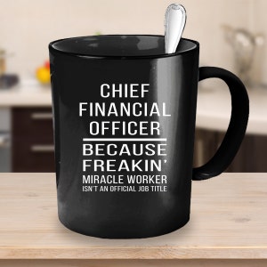 Op de afbeelding: Zwarte koffiemok met witte tekst die luidt: "Chief Financial Officer Because Freakin' Miracle Worker Isn't An Official Job Title"