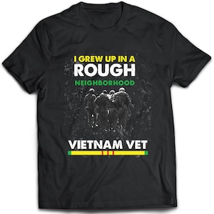 May include: Black t-shirt with a distressed graphic design featuring a group of soldiers walking in formation. The text "I grew up in a rough neighborhood" and "Vietnam Vet" are printed on the shirt. A yellow and green stripe is printed below the text.