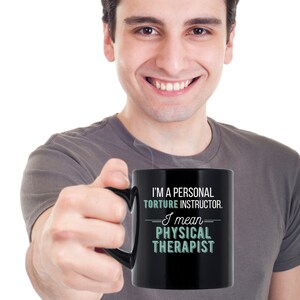 May include: A black coffee mug with white text that reads "I'm a personal torture instructor. I mean physical therapist."