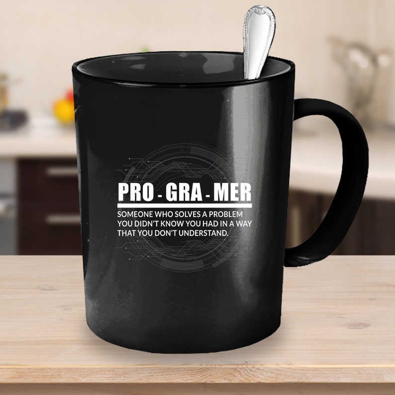Puede incluir: Taza de caf&eacute; negra con un dise&ntilde;o blanco que dice "PRO-GRA-MER" y "SOMEONE WHO SOLVES A PROBLEM YOU DIDN'T KNOW YOU HAD IN A WAY THAT YOU DON'T UNDERSTAND."