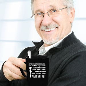 May include: Black coffee mug with white text that reads "IT CAN NOT BE INHERITED nor can it ever be purchased I HAVE EARNED IT WITH MY BLOOD, TEARS & SWEAT I OWN IT FOREVER the title VIETNAM VET". A silver spoon rests inside the mug.