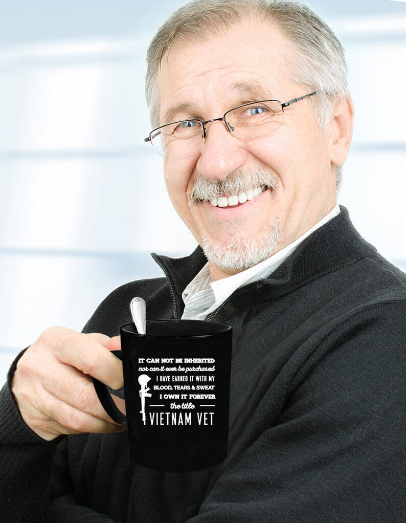 May include: Black coffee mug with white text that reads "IT CAN NOT BE INHERITED nor can it ever be purchased I HAVE EARNED IT WITH MY BLOOD, TEARS & SWEAT I OWN IT FOREVER the title VIETNAM VET". A silver spoon rests inside the mug.