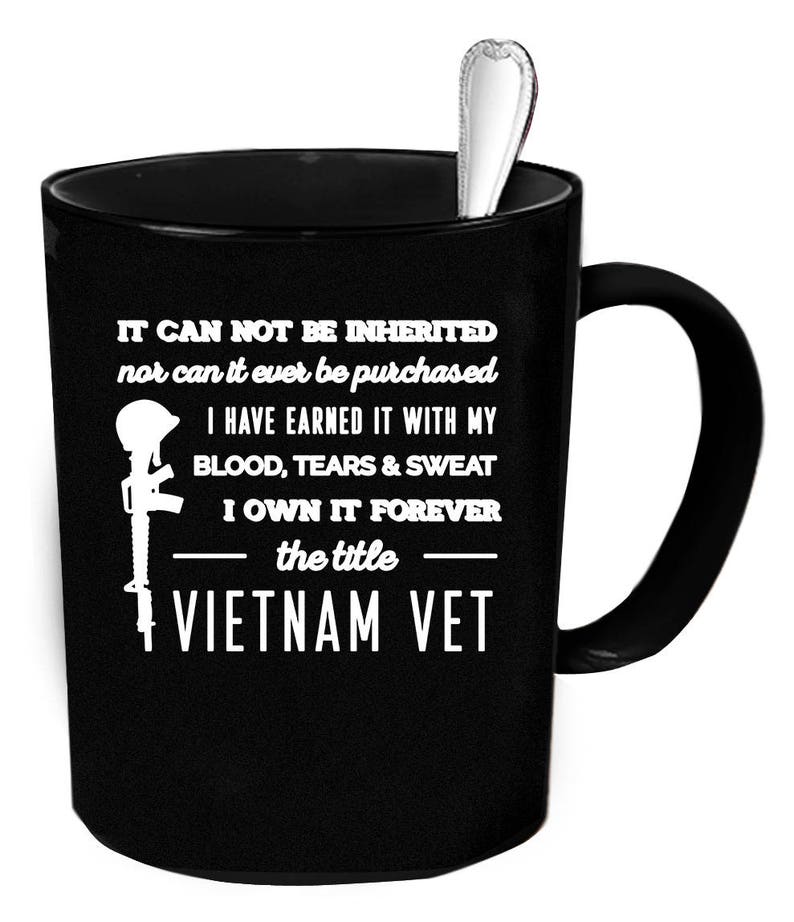 May include: Black ceramic mug with a silver spoon inside. The mug features white text and a graphic of a helmet and rifle, with the words "VIETNAM VET". The text reads "IT CAN NOT BE INHERITED...I OWN IT FOREVER".