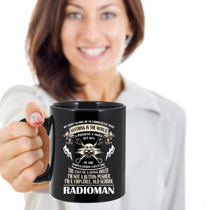 May include: Black coffee mug with a white design featuring a skull with wrench and lightning bolt graphics. The text reads "My craft allows me to communicate with anything in the world. I possess a skill set 98% of the population can't do. The last of a dying breed. I'm not a button pusher. I'm a 100% true, old school Radioman."