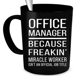 Op de afbeelding: Zwarte koffiemok met witte tekst die "Office Manager Because Freakin' Miracle Worker Isn't An Official Job Title" zegt