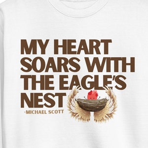 May include: White sweatshirt with brown text that reads "My heart soars with the eagle's nest - Michael Scott". A small cartoon eagle is in a nest with wings spread.