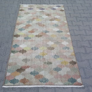 May include: A rectangular rug with a repeating pattern of colorful, stylized floral shapes in shades of pink, yellow, blue, and brown. The rug has a beige background and a fringed edge. The rug is approximately 3 feet wide and 5 feet long.