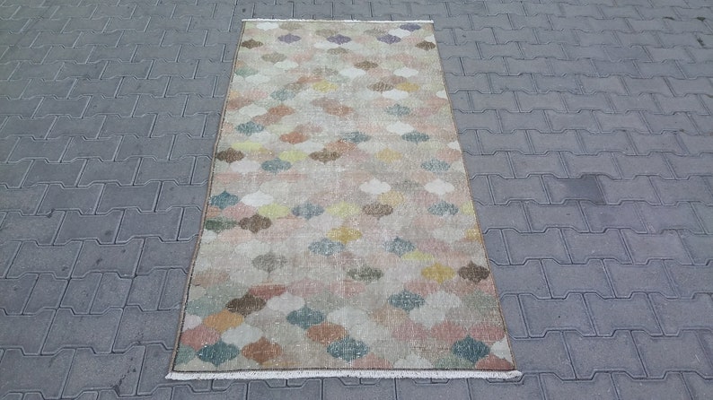 May include: A rectangular rug with a repeating pattern of colorful, stylized floral shapes in shades of pink, yellow, blue, and brown. The rug has a beige background and a fringed edge. The rug is approximately 3 feet wide and 5 feet long.