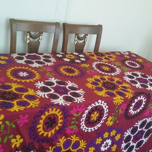 Puede incluir: Un mantel rojo con un patr&oacute;n bordado de colores de c&iacute;rculos y flores. El mantel est&aacute; puesto sobre una mesa de madera con cuatro sillas.