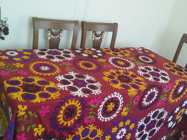 Puede incluir: Un mantel rojo con un patr&oacute;n bordado de colores de c&iacute;rculos y flores. El mantel est&aacute; puesto sobre una mesa de madera con cuatro sillas.