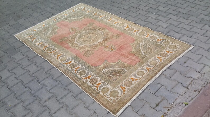 Puede incluir: Alfombra rectangular con un campo central rosa y un borde detallado. La alfombra presenta una paleta de colores beige y marr&oacute;n con dise&ntilde;os florales y geom&eacute;tricos. Se encuentra sobre una superficie de ladrillos grises.