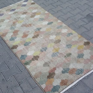 May include: A rectangular rug with a repeating pattern of colorful, cloud-like shapes in shades of pink, yellow, blue, and brown. The rug has a beige background and a fringed edge. The rug is likely made of woven material.