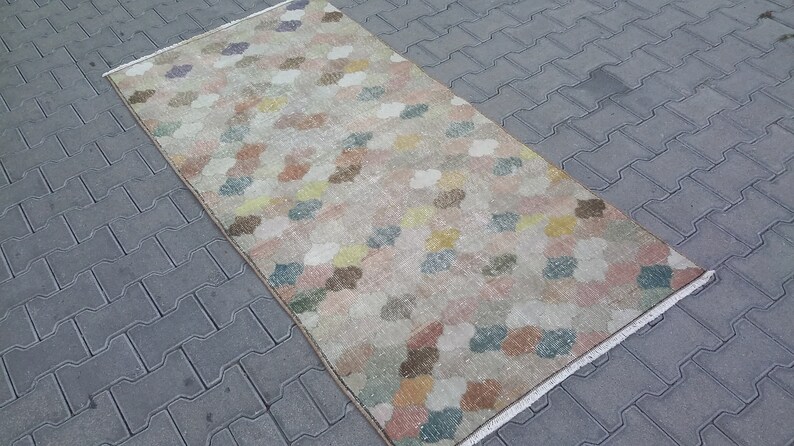 May include: A rectangular rug with a repeating pattern of colorful, cloud-like shapes in shades of pink, yellow, blue, and brown. The rug has a beige background and a fringed edge. The rug is likely made of woven material.