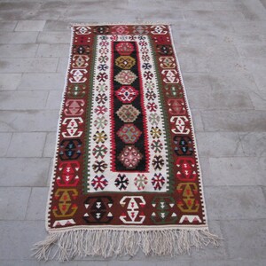 May include: A traditional Turkish rug with a white background and intricate geometric patterns in red, blue, green, and brown. The rug has a fringe border.