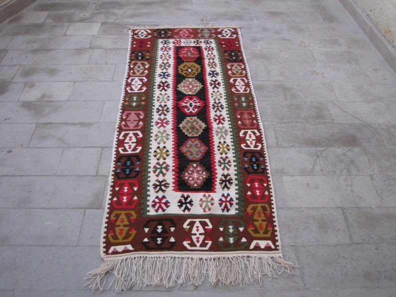 May include: A traditional Turkish rug with a white background and intricate geometric patterns in red, blue, green, and brown. The rug has a fringe border.