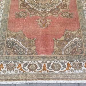 Puede incluir: Una alfombra rectangular de estilo vintage con un campo central de color coral descolorido. La alfombra presenta un borde ornamentado con patrones florales y geom&eacute;tricos en tonos beige, gris y naranja. El dise&ntilde;o de la alfombra es sim&eacute;trico y detallado.