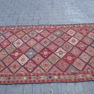 May include: A red, beige, and blue patterned rug with a diamond design. The rug has a fringe border.