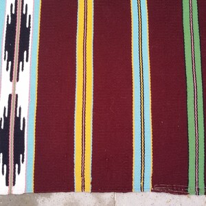 May include: A striped woven rug with a burgundy background. The rug has stripes of yellow, light blue, dark blue, green, and pink.