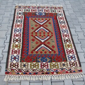 May include: A traditional Turkish rug with a colorful geometric pattern in shades of red, blue, green, and white. The rug has a fringe border and is woven with intricate details.