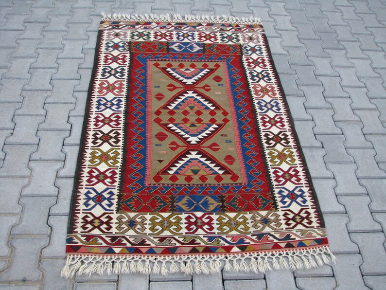 May include: A traditional Turkish rug with a colorful geometric pattern in shades of red, blue, green, and white. The rug has a fringe border and is woven with intricate details.