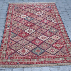 May include: A traditional red, beige, and blue patterned rug with a geometric design. The rug has a fringe border.