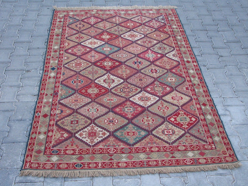 May include: A traditional red, beige, and blue patterned rug with a geometric design. The rug has a fringe border.