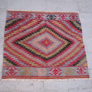 May include: A colorful rug with a diamond pattern in shades of red, black, yellow, and gray. The rug has a fringe border.