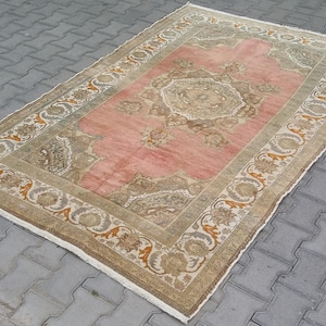 Puede incluir: Alfombra rectangular con un campo central rosa y patrones florales beige y marr&oacute;n ornamentados. El borde presenta un dise&ntilde;o similar con detalles en naranja. La alfombra est&aacute; colocada sobre una superficie de ladrillos grises.