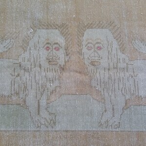 以下が含まれることがあります： ベージュの敷物に、赤い目をした白いライオンが2匹刺繍されている