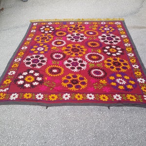 Puede incluir: Un tapiz de pared de tela roja con un patr&oacute;n floral. El patr&oacute;n presenta flores blancas, amarillas, rosas, moradas y negras en un dise&ntilde;o circular.