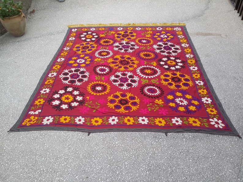 Puede incluir: Un tapiz de pared de tela roja con un patr&oacute;n floral. El patr&oacute;n presenta flores blancas, amarillas, rosas, moradas y negras en un dise&ntilde;o circular.