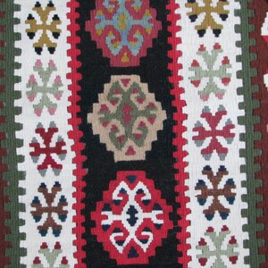 May include: A close-up of a colorful woven rug with intricate geometric patterns in shades of red, green, white, and brown.