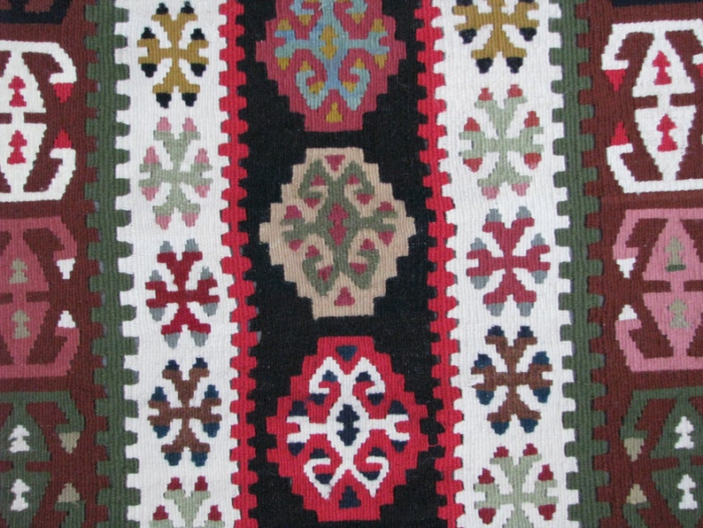 May include: A close-up of a colorful woven rug with intricate geometric patterns in shades of red, green, white, and brown.