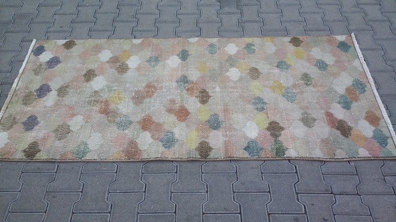 May include: Rectangular rug with a repeating quatrefoil pattern in pastel colors. The rug features a beige background with colorful quatrefoils in shades of pink, blue, yellow, and brown. The rug has a distressed, vintage look.