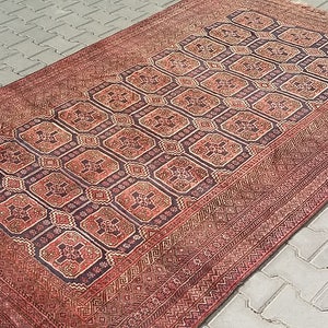 Puede incluir: Una alfombra rectangular, tejida a mano, con un patrón geométrico central en tonos rojos, marrones y azul oscuro. La alfombra presenta un borde detallado y una apariencia vintage desgastada, adecuada para la decoración del hogar.